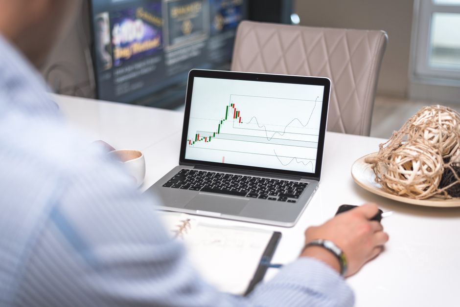 Man reviewing financial analysis on laptop in a modern office setting with focus on trading charts and data.