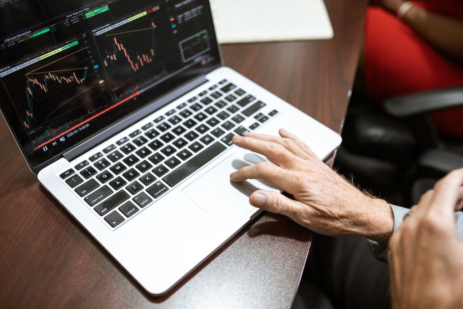 Close-up of hand using laptop for stock market analysis in office setting.